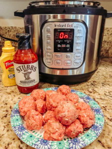 Raw meatballs on a plate in front of an instant pot.