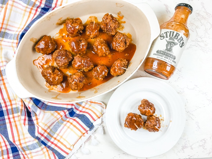 A plate of instant pot meatballs next to a bottle of stubb's BBQ sauce.