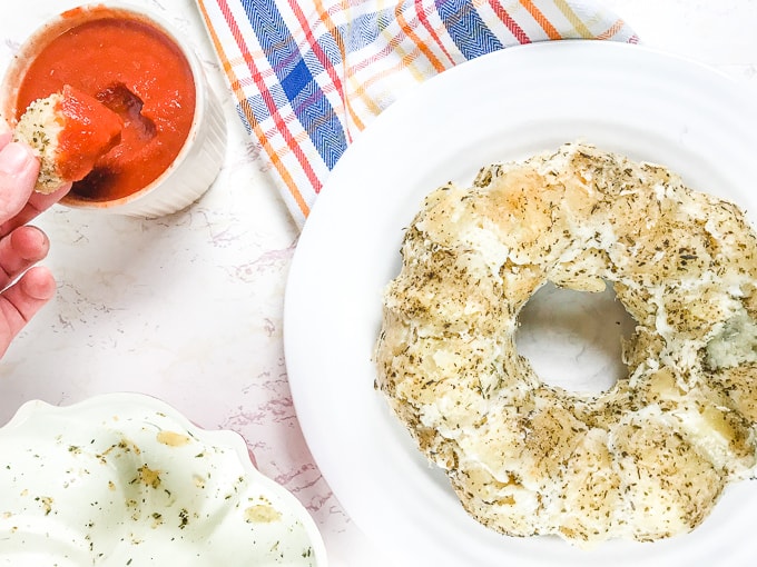 A hand dipping a piece of pull apart pizza bread into pizza sauce.