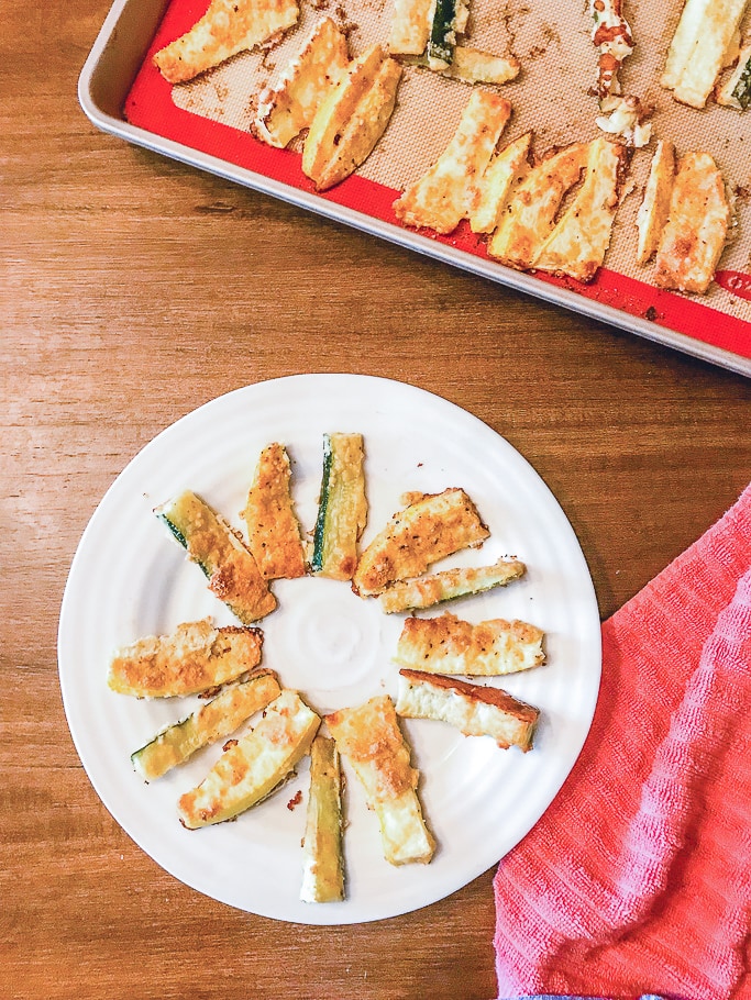 Zucchini fries on a plate next to a red towel.