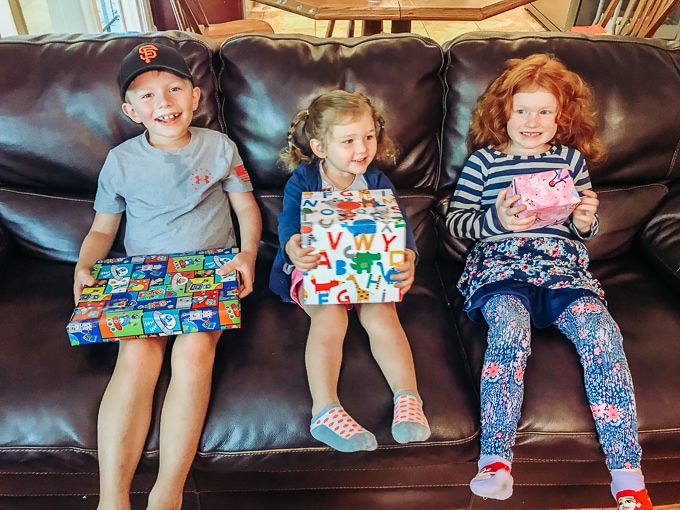Three kids sitting on a black couch, holding their wrapped gifts.