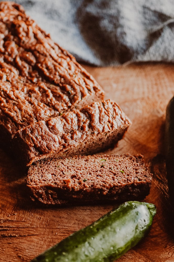 A loaf of gluten free zucchini bread sliced on a cutting board.