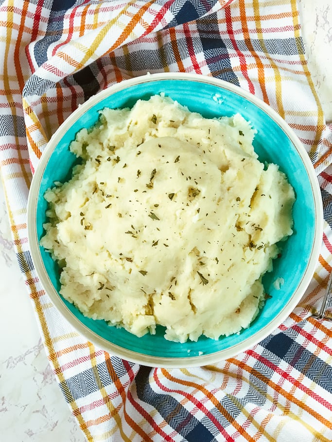 A bowl of instant pot garlic mashed potatoes on top of a red, blue, and white plaid towel.