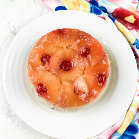 instant pot pineapple upside down cake on a white plate next to a blue floral towel.