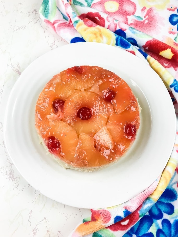 instant pot pineapple upside down cake on a white plate next to a blue floral towel.