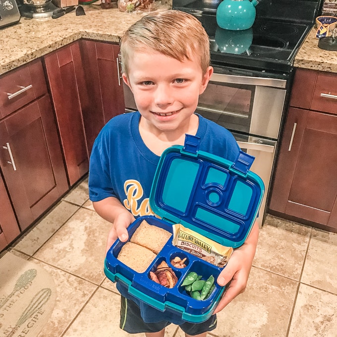 Little boy smiling and holding a bento box.