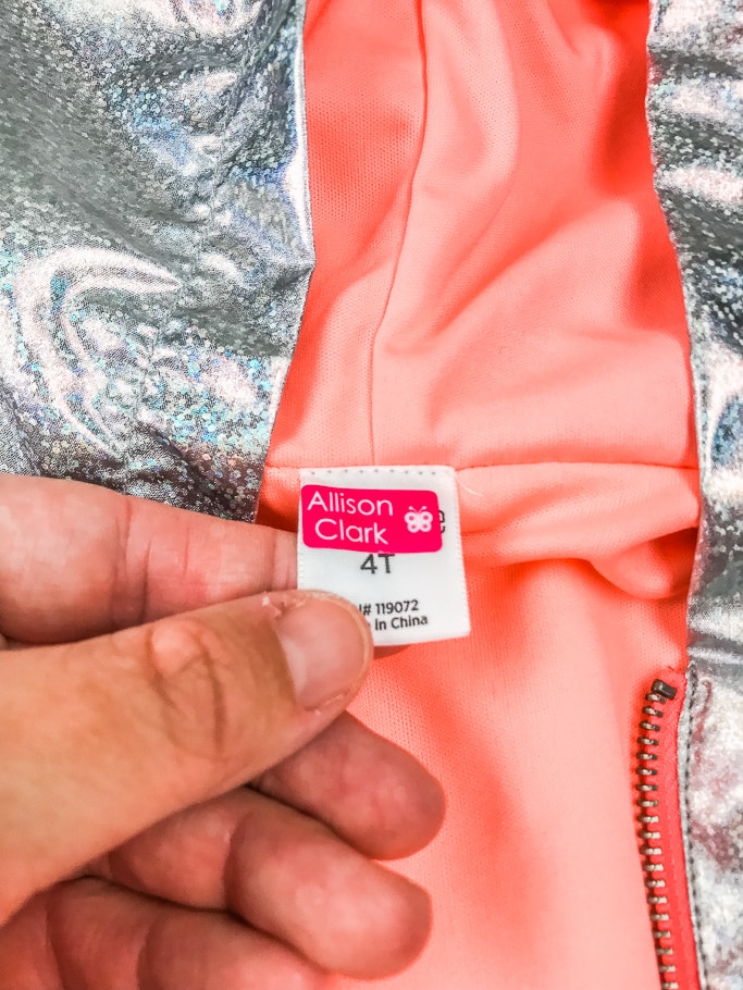 A hand holding a kid's jacket label with a name label stuck on it.