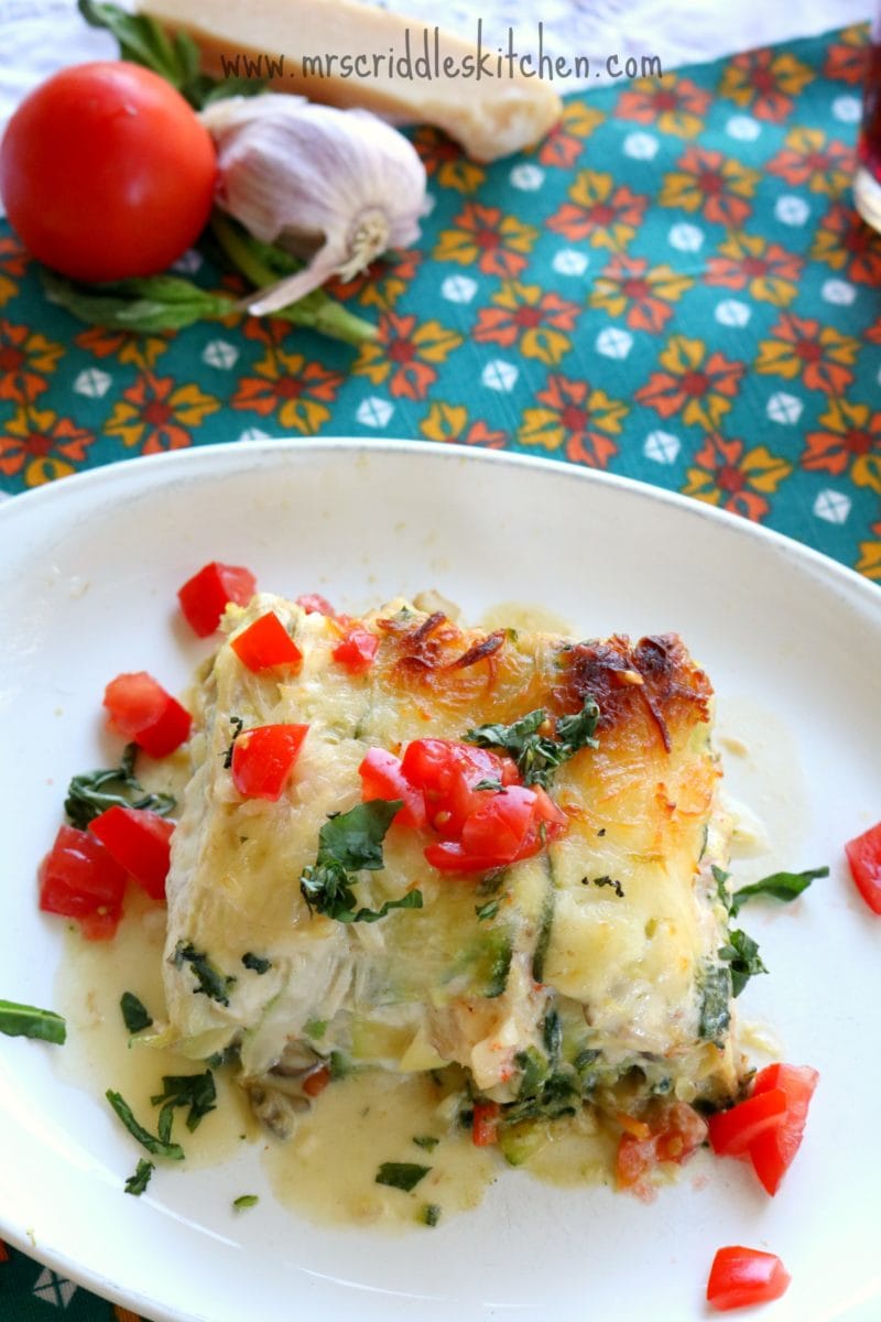 Seafood lasagna with zucchini on a white plate and topped with diced tomatoes. 