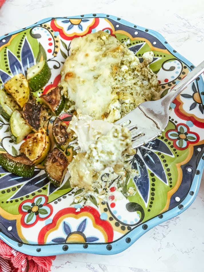 A bite of creamy pesto chicken on a fork resting on the plate of food.