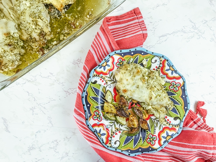 A glass casserole dish filled with creamy pesto chicken and next to a plate served with pesto chicken bake.