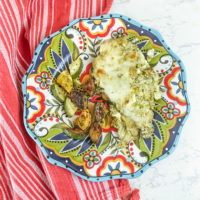 A red striped towel under a colorful plate topped with creamy pesto chicken and roasted zucchini.