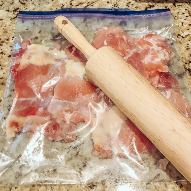 A rolling pin thinning out chicken thighs in a bag.