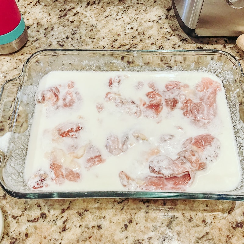 Chicken thighs soaking In a dish of buttermilk.