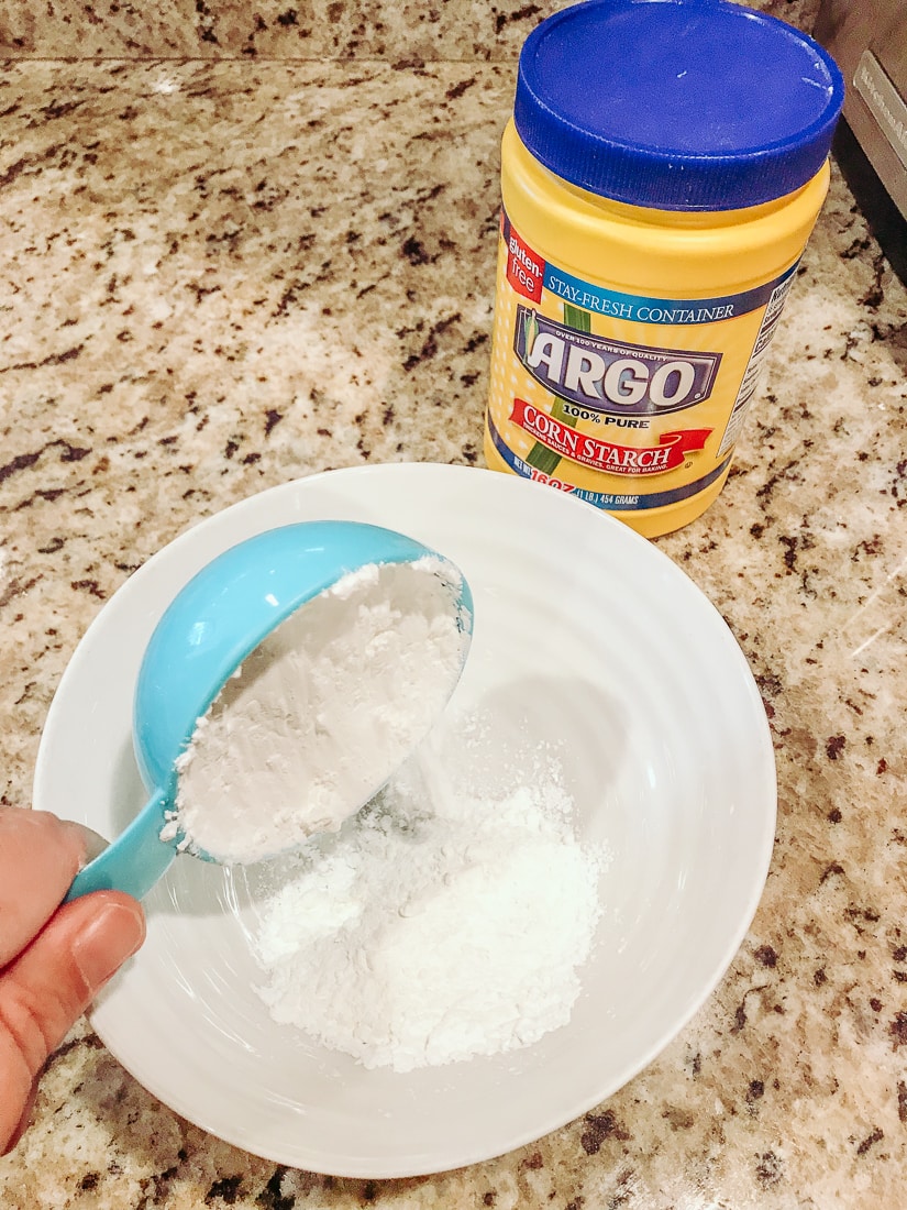 A measuring cup pouring Argo Corn Starch into a white bowl.