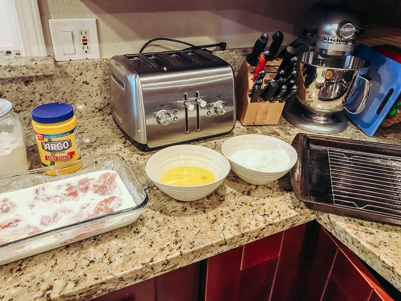 A photo of a kitchen counter set up to make crispy chicken thighs with bowls of egg and a bowl of crispy coating.