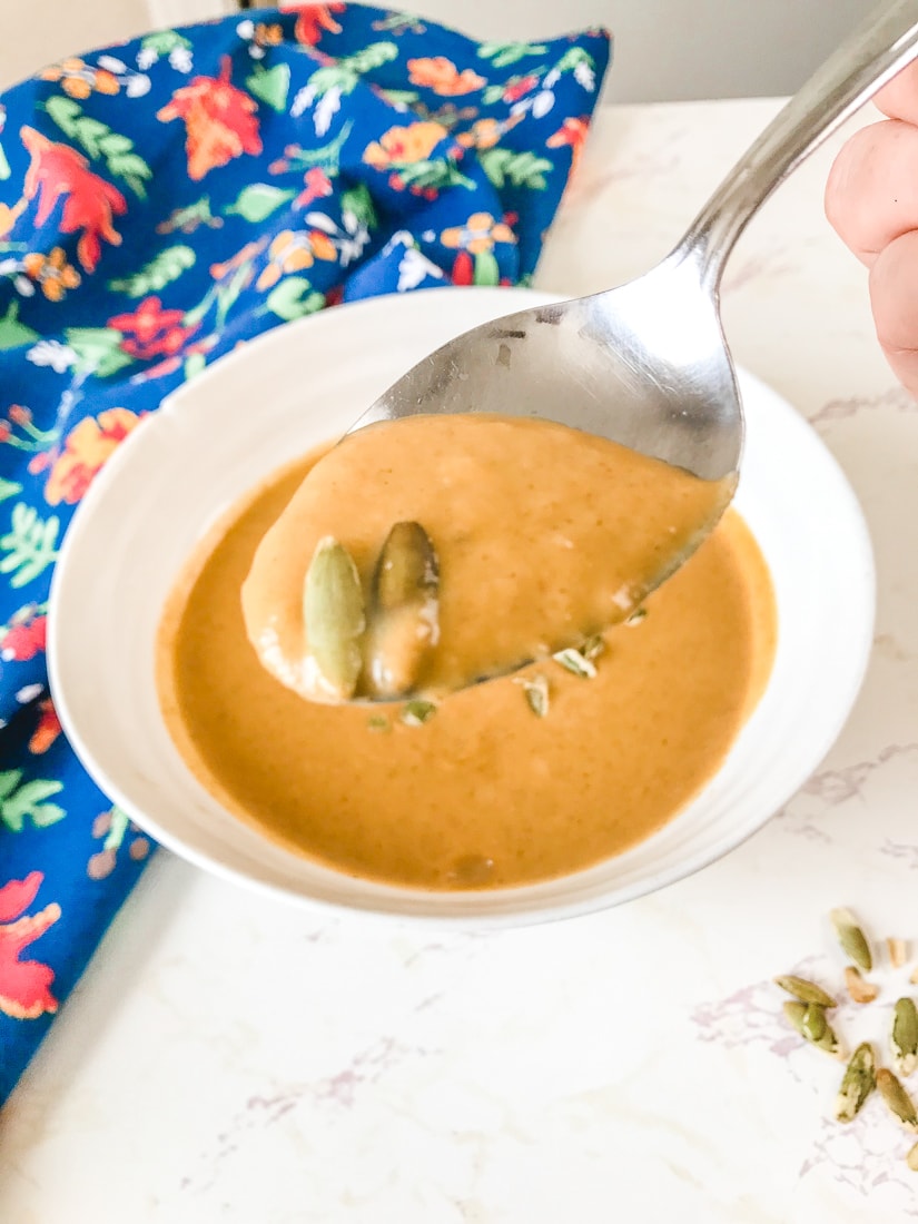 A spoonful of easy pumpkin soup over a white bowl of soup and a blue dish towel.
