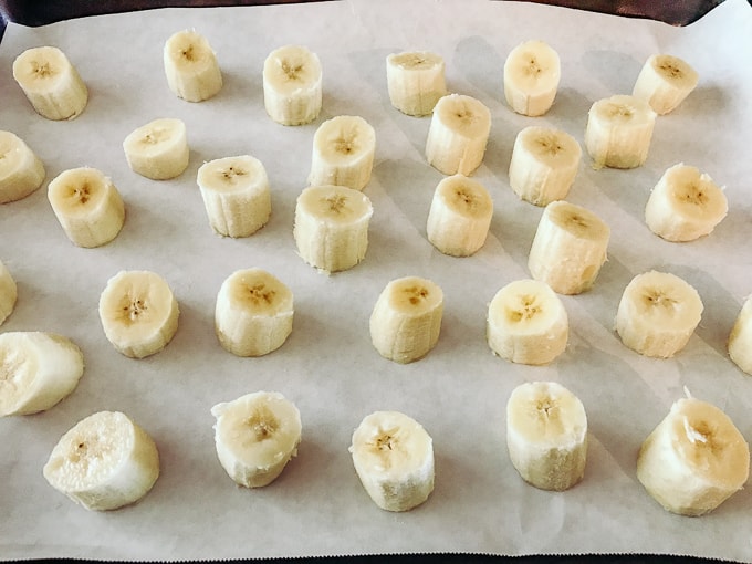 Sliced bananas on a cookie sheet as part of our tutorial on how to freeze bananas.