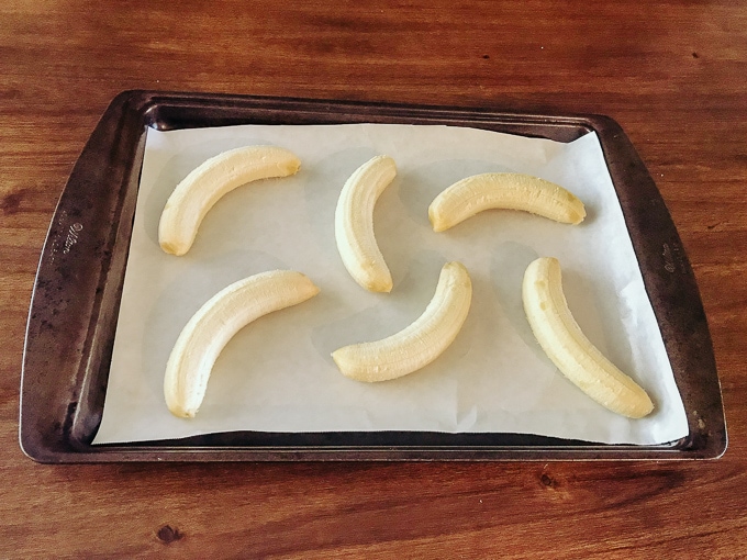 Six peeled bananas on a cookie sheet.