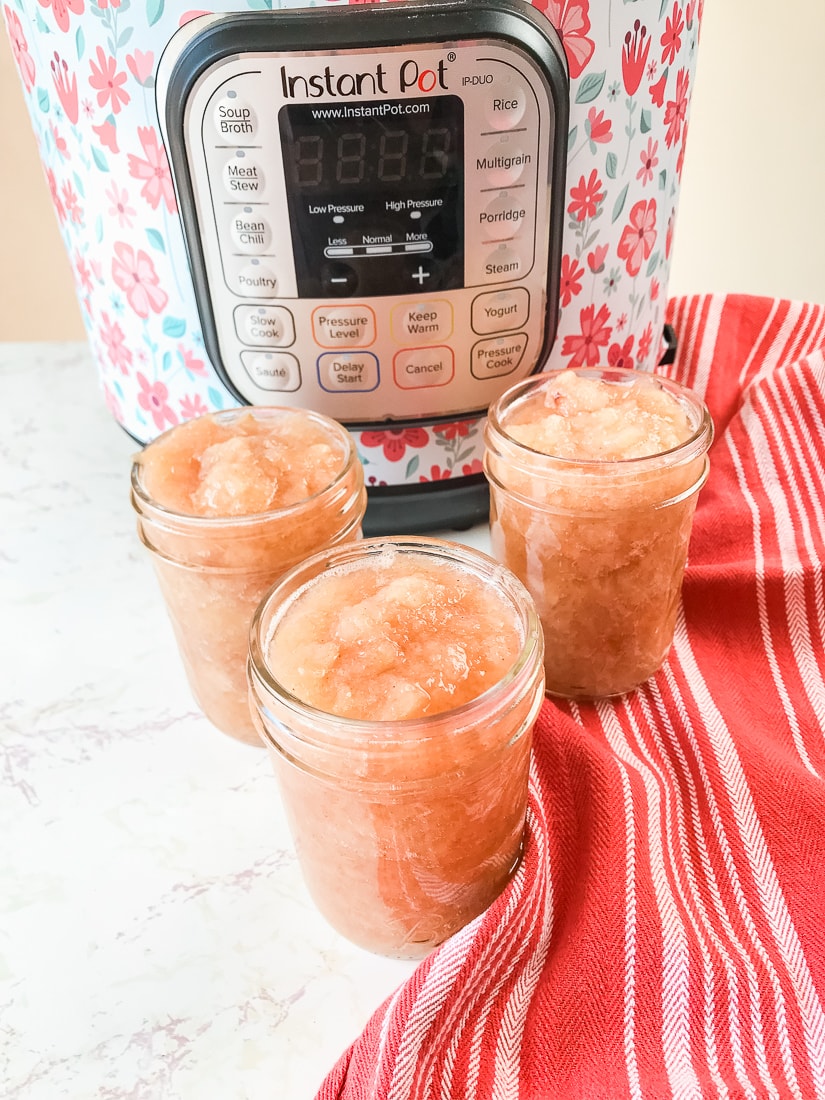 Three jars of pressure cooker applesauce in front of an instant pot.