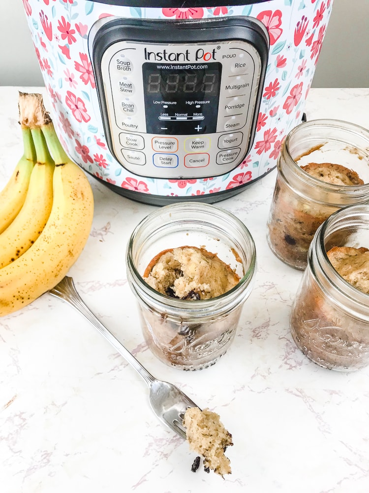 A bite of pressure cooker banana bread on a fork in front of a bunch of bananas and instant pot.