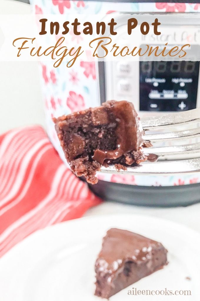A bite of instant pot brownies from scratch held up in front of an instant pot.