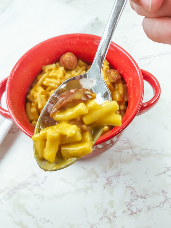 A bite of instant pot Kraft Mac and cheese over a red bowl that says yummy.