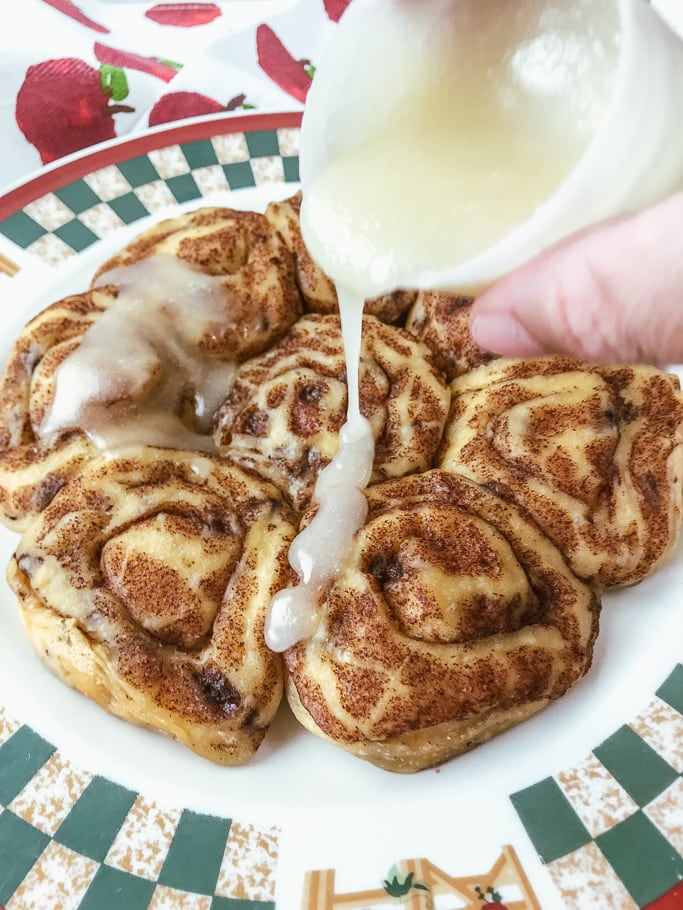 Icing being poured over a plate of instant pot Pillsbury cinnamon rolls.