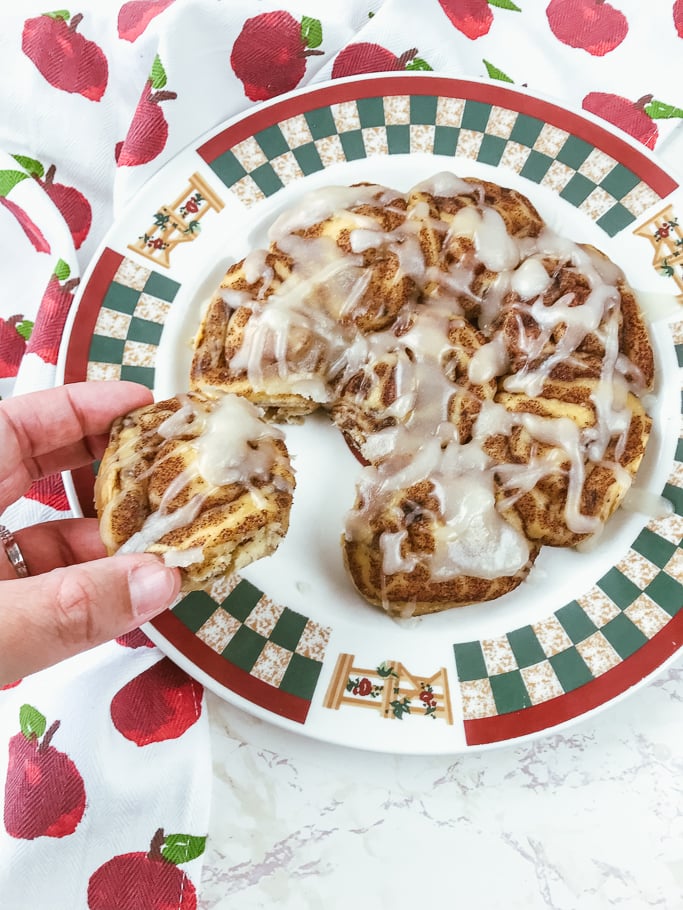 A hand pulling a cinnamon roll away from a plate of pressure cooker pillsbury cinnamon rolls.