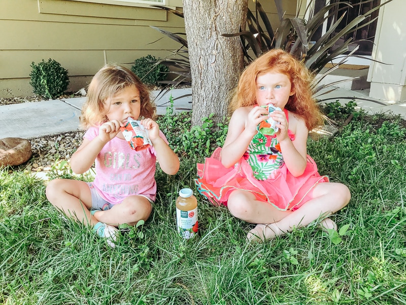 Two girls sitting outside and snacking on applesauce patches.