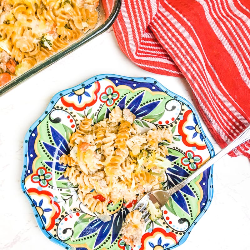 A colorful plate with a serving of turkey noodle casserole next to a red striped dish towel.