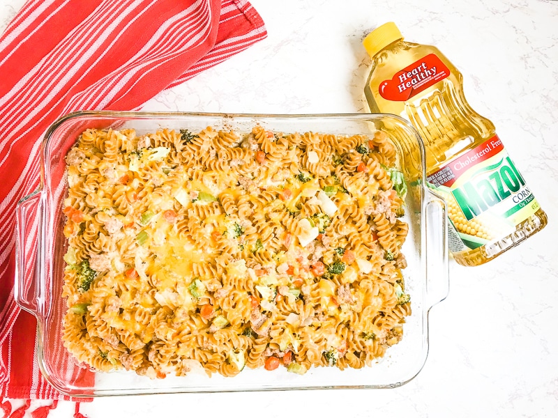 Baked turkey noodle casserole in a glass casserole dish next to a bottle of Mazola Corn Oil.