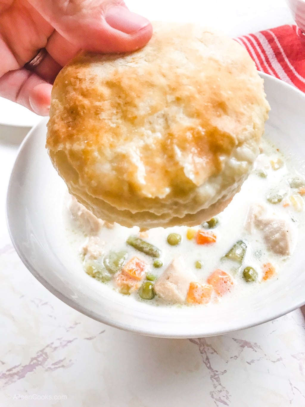 A hand holding up a biscuit that was just dunked in instant pot chicken pot pie soup.