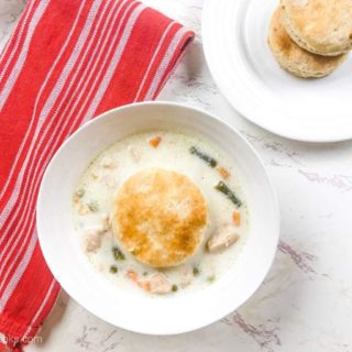 A white bowl filled with instant pot chicken pot pie soup and topped with a biscuit next to a red striped towel.