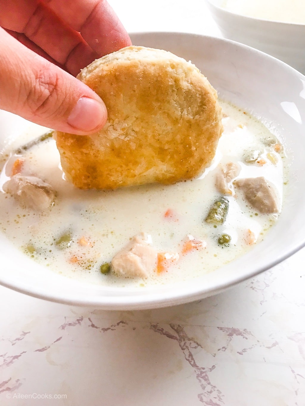 A biscuit being dunked into pressure cooker chicken pot pie soup.