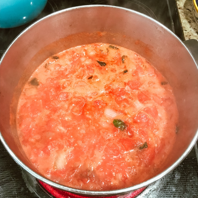 A pot full of the ingredients for the creamy tomato basil soup recipe, mainly tomatoes and basil.