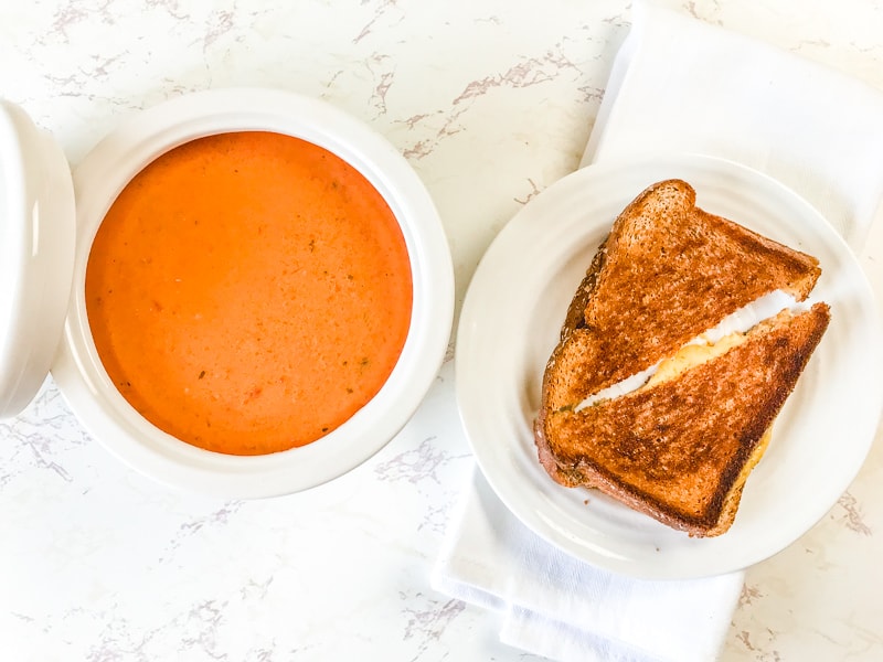 A bowl of tomato basil soup next to a grilled cheese.