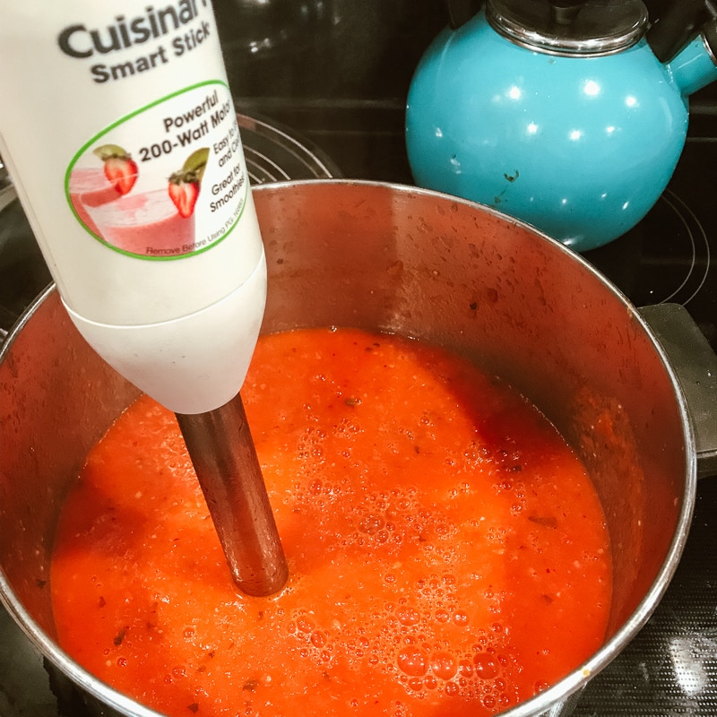 Creamy tomato basil soup being pureed by an immersion belender.