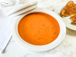 Bowl of creamy tomato basil soup on a white counter.