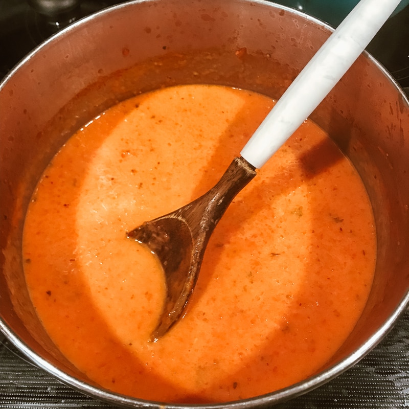 A wooden spoon mixing heavy cream into tomato basil soup.