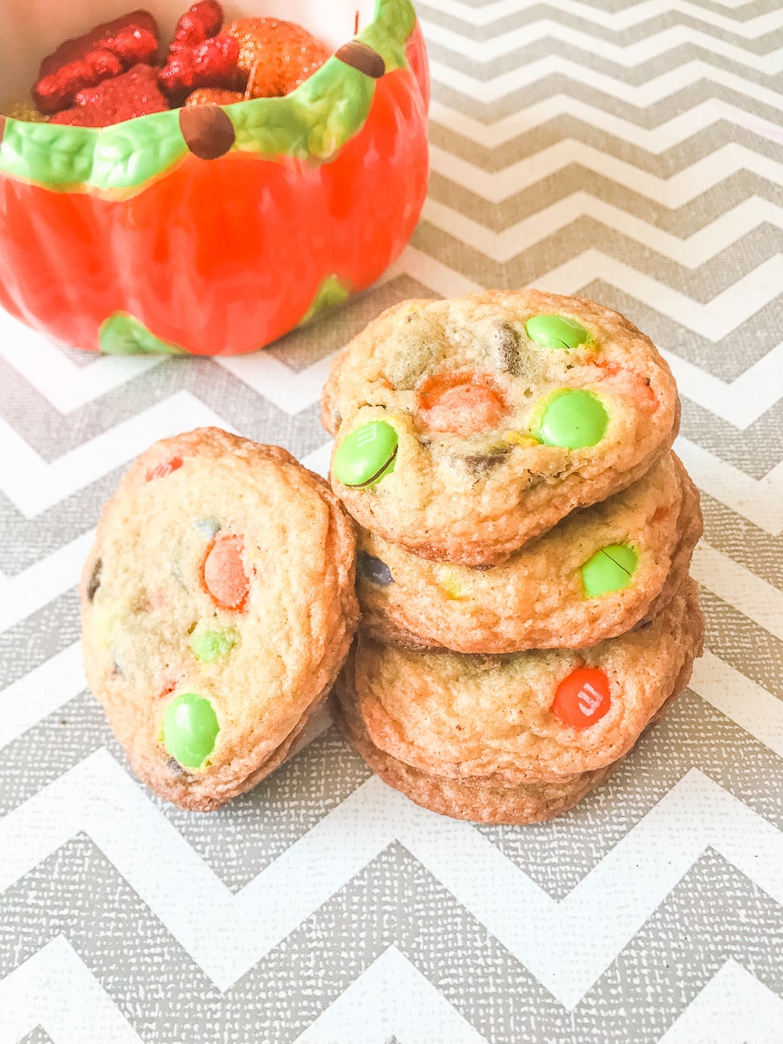 A stack of three halloween M&M cookies with one cookie leaning on the tower of cookies.