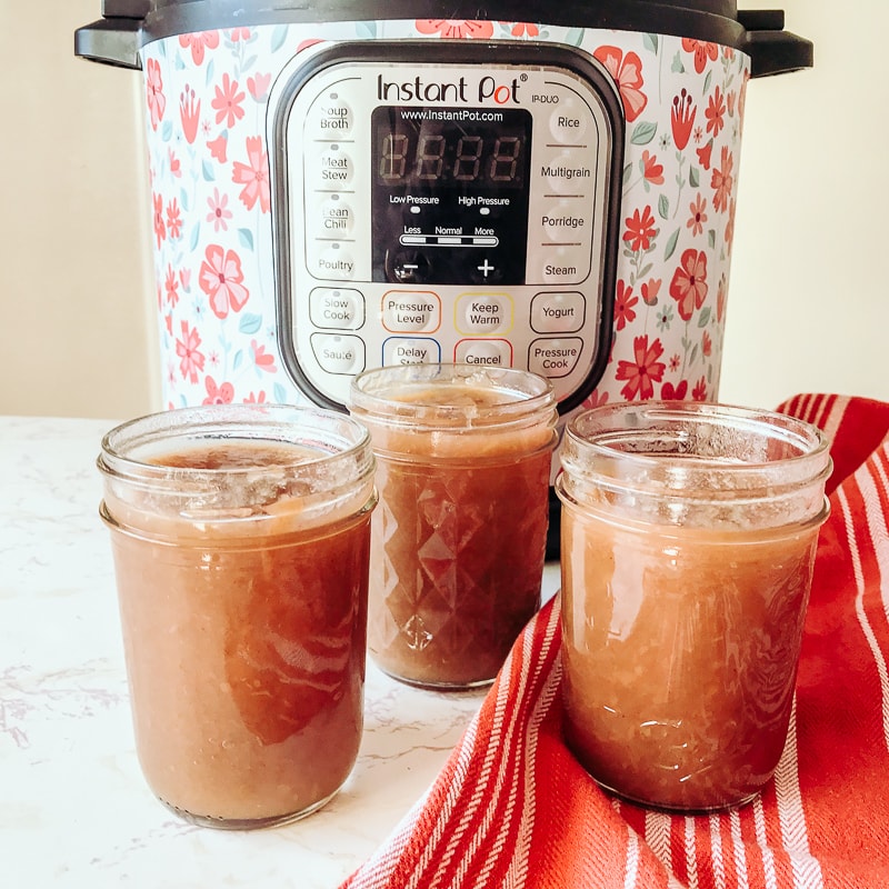 Three jars of instant pot apple butter in front of a pressure cooker.