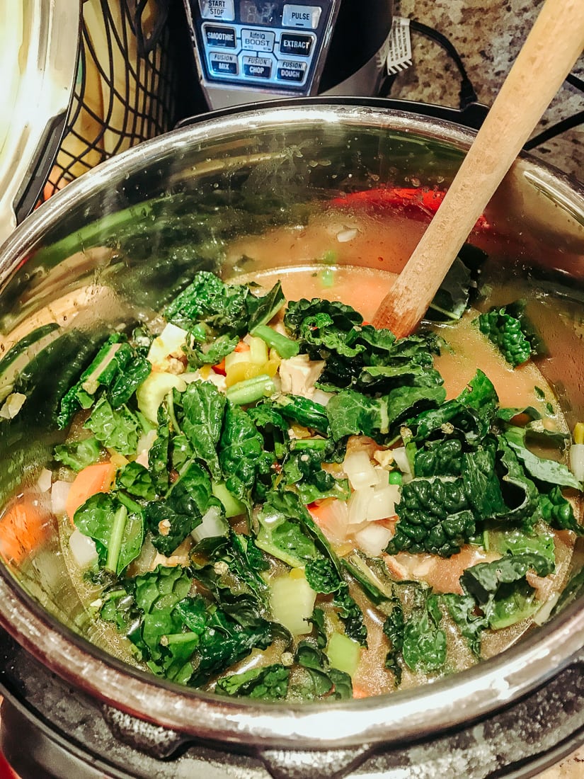 Chicken broth, vegetables, and chicken being stirred for instant pot chicken vegetable soup.