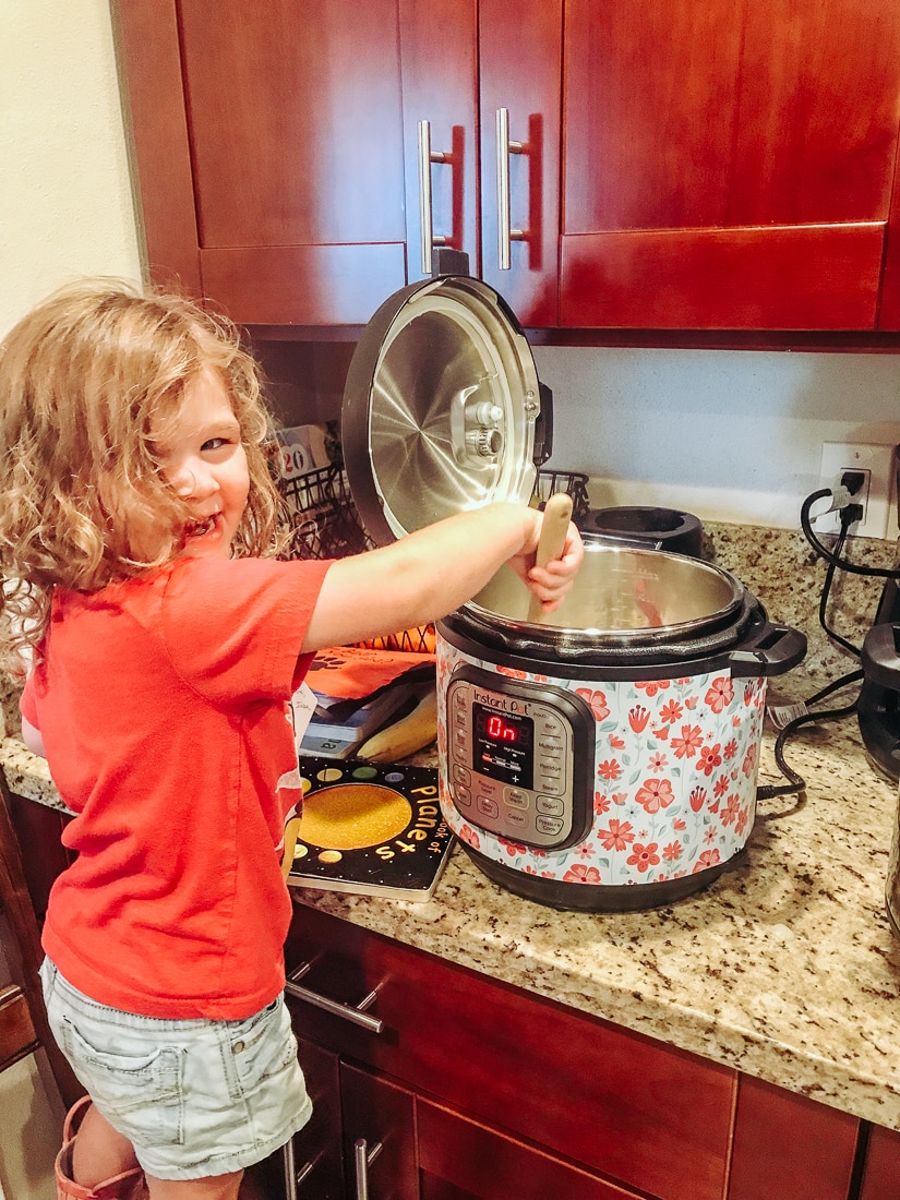 Little girl stirring onion and garlic in an instant pot.