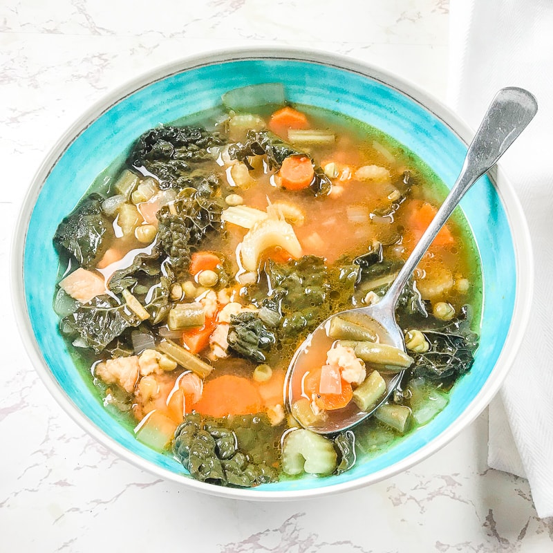 A bowl of pressure cooker chicken and vegetable soup with a spoon sticking out of the bowl.