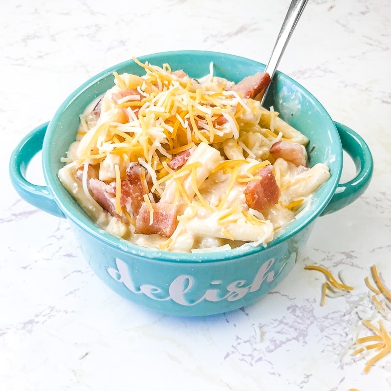 A teal bowl filled with instant pot crack chicken pasta topped with shredded cheese and bacon bits.