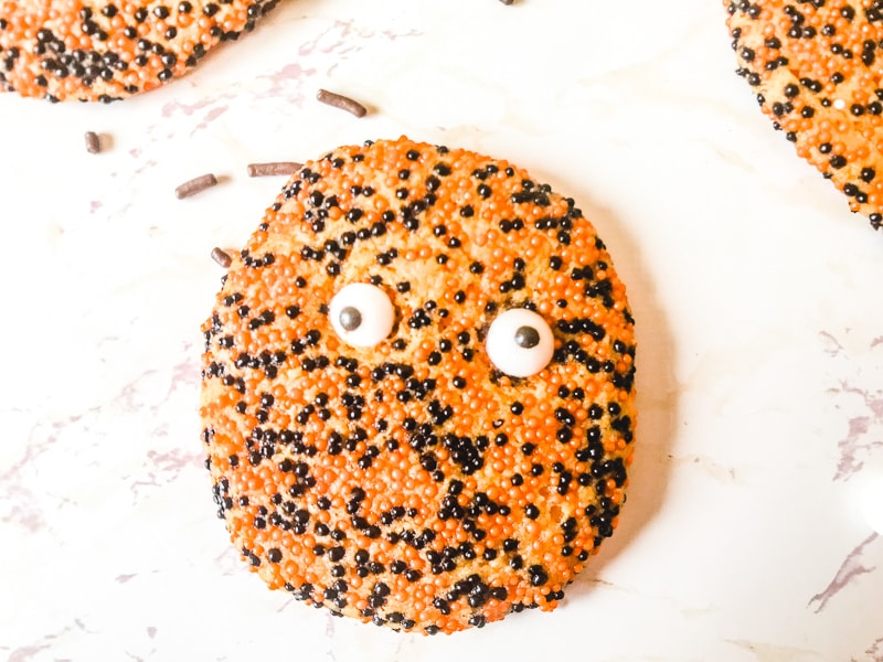Close up of a orange and black halloween cookie with candy eyes.