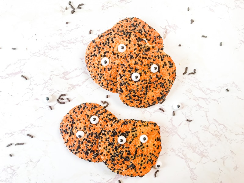 Four orange and black monster sprinkle halloween cookies on a white background. 