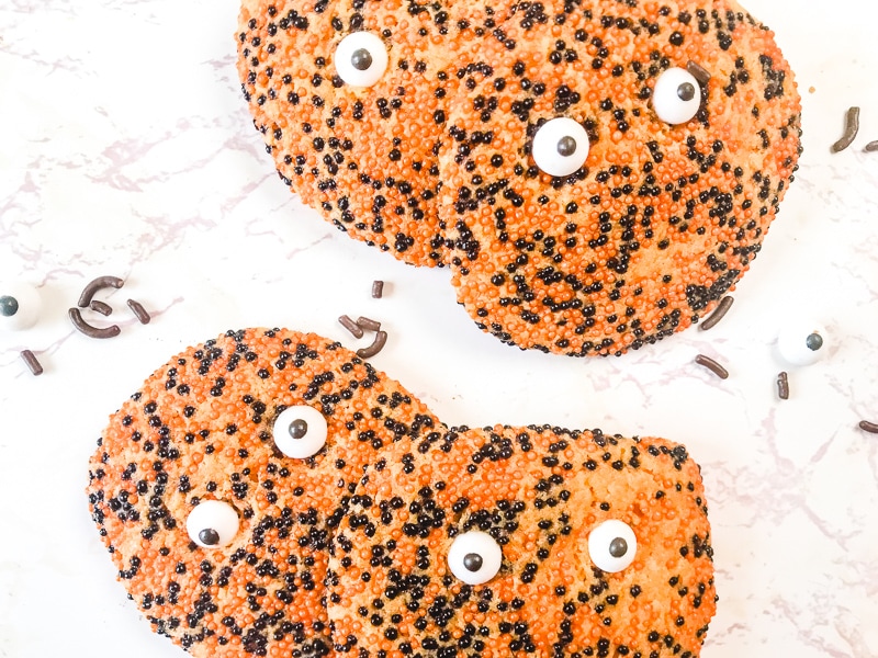 Four spooky halloween cookies surrounded by loose black sprinkles and candy eyes.
