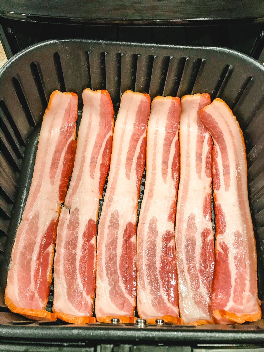 6 slices of uncooked bacon in an even layer inside the basket of an air fryer.