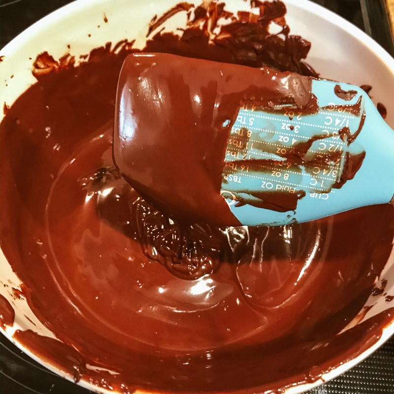 A blue spoon dipping into a bowl of melted chocolate. 